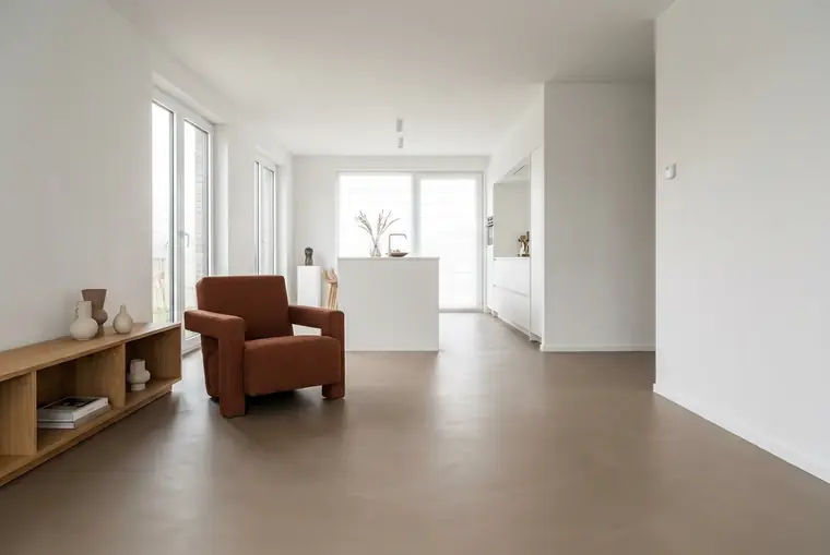 Séjour dont le sol en béton ciré gris taupe court sans joint jusqu’à la cuisine ouverte